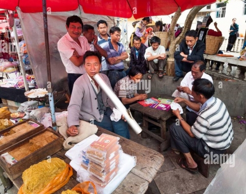 homme-fumant-pipe-triditionnelle-entoure-d-un-groupe-d-hommes-jouant-aux-cartes-sur-un-etal-de-marche-de-vendeurs-de-tabac-dans-le-yunnan.jpg